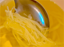 A close-up of Egg Drop Soup in a bowl, with a spoon scooping up some of the silky egg ribbons