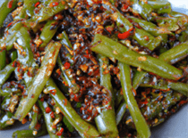 A plate of spicy green beans with visible chili flakes and Sichuan peppercorns